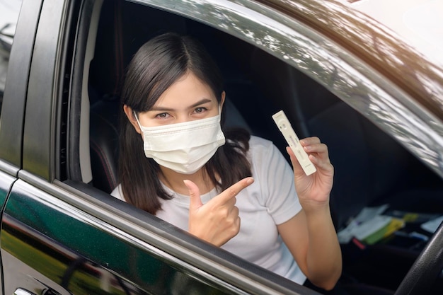 Una donna che tiene l'atk in auto esegue un test di autoraccolta per un test di salute e sicurezza COVID19