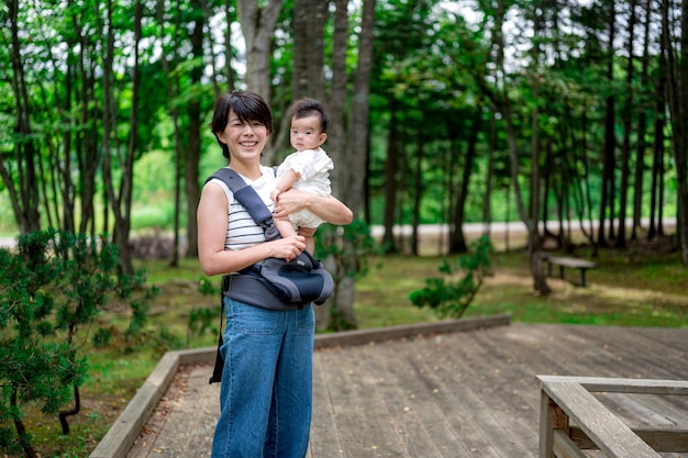 Una donna che tiene un bambino in un marsupio in una foresta