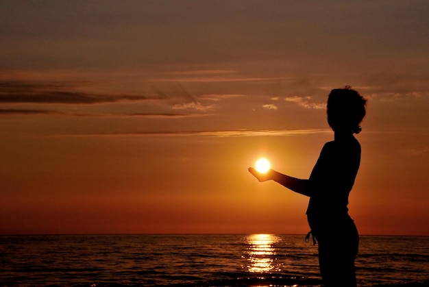 Una donna che tiene un sole davanti a un tramonto