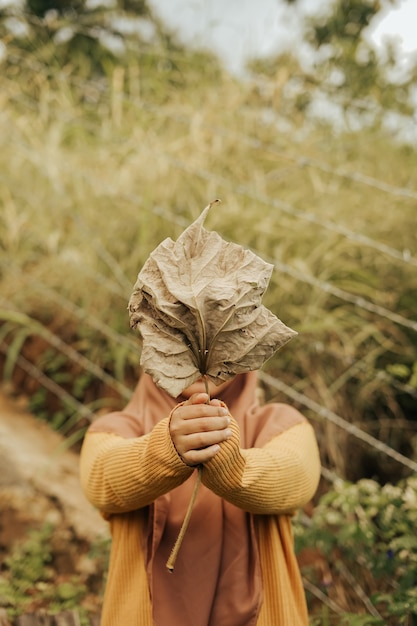 una donna che tiene una grande foglia che gli copre il viso