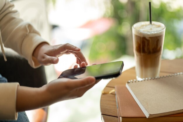 Una donna che usa il suo smartphone mentre è seduta vicino alla finestra di un bar e manda messaggi ai social media