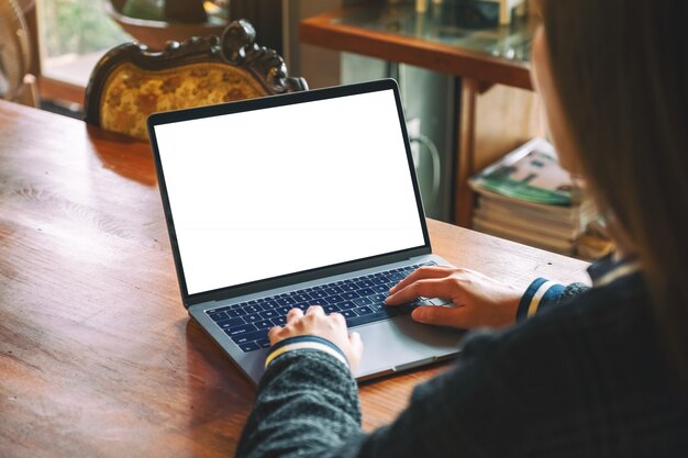 una donna che usando e digitando sulla tastiera del computer portatile con lo schermo del desktop bianco bianco sul tavolo di legno