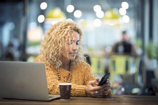 Una donna che utilizza il telefono e il laptop seduto al bar nella sala d'attesa del gate dell'aeroporto Viaggi alternativi e stile di vita lavorativo Uomini d'affari che utilizzano la connessione wireless gratuita e lavorano in un ufficio alternativo