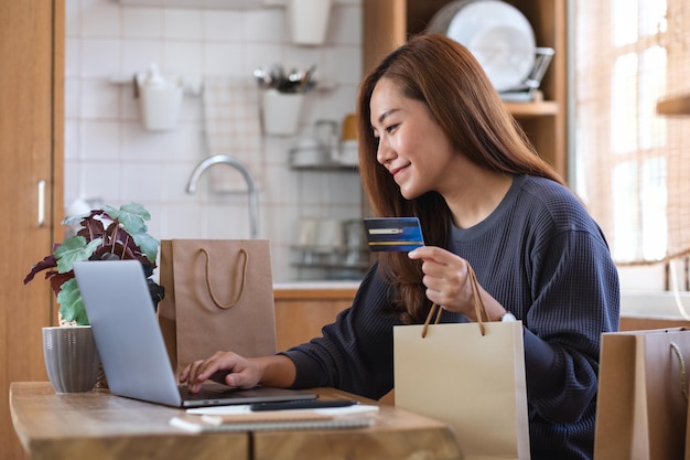 Una donna che utilizza un computer portatile e una carta di credito per lo shopping online a casa