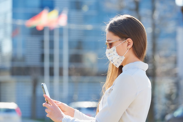 Una donna che utilizza uno smartphone indossa una maschera medica per evitare la diffusione del coronavirus in una strada cittadina