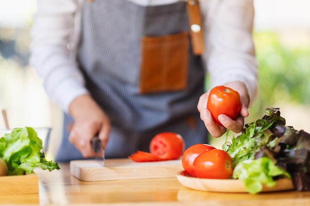 Una donna chef che tiene e raccoglie un pomodoro fresco da un vassoio di verdure sul tavolo