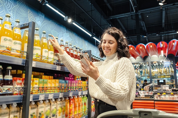 Una donna compra del succo da una lista della spesa sul suo telefono in un supermercato