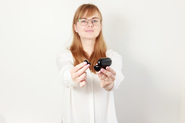 Una donna con gli occhiali in possesso di cuffie portatili su sfondo bianco