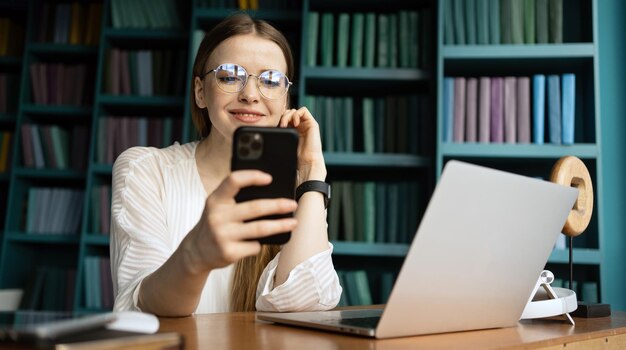 Una donna con gli occhiali scrive un messaggio in una chat lavora utilizza un telefono in un ufficio in uno spazio di coworking