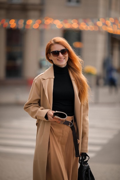 una donna con gli occhiali scuri e una rivista in mano cammina per strada. camminare nella città d'autunno