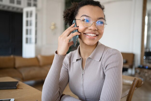 Una donna con gli occhiali sta parlando al telefono in ufficio distogliendo lo sguardo e sorridendo