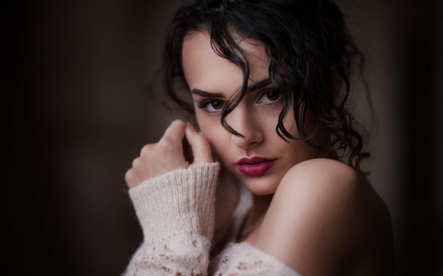 una donna con i capelli lunghi e un top bianco senza maniche sta posando con la mano sul mento