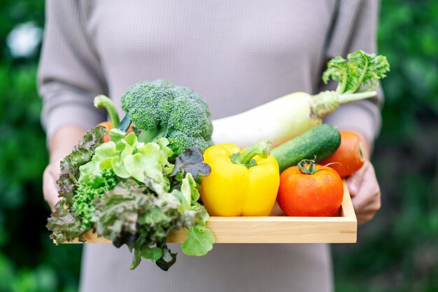 Una donna con in mano un misto di verdure fresche in un vassoio di legno