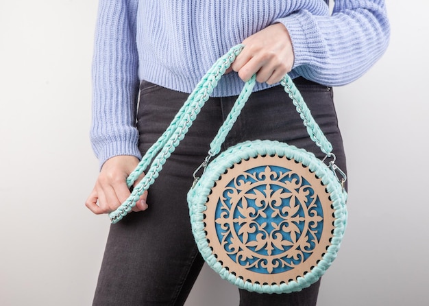 Una donna con in mano una borsa rotonda con un top blu e una camicia bianca.