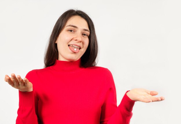 Una donna con le pillole sulla lingua allarga le braccia su uno sfondo bianco.