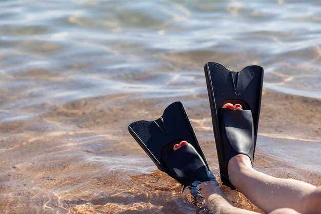 Una donna con le pinne nere schizza vicino alla riva. Le pinne sporgono dall'acqua. Attrezzatura per il nuoto.