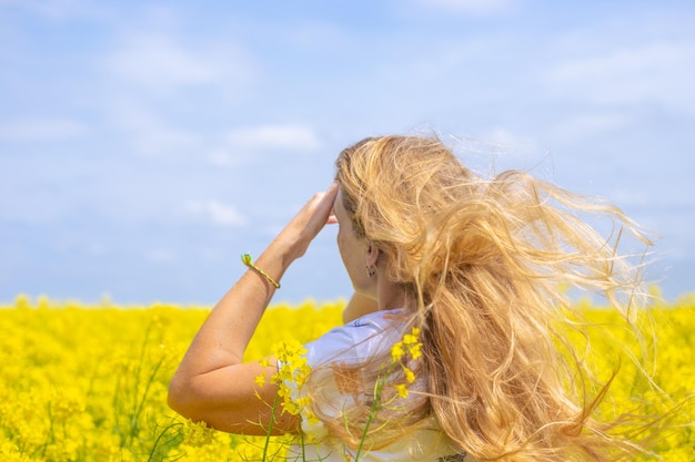 Una donna con lunghi capelli biondi che si sviluppano nel vento in un campo di colza in fiore in una soleggiata giornata primaverile