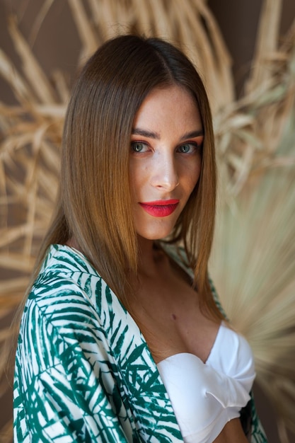 Una donna con lunghi capelli castani e una foglia di palma verde sulla parte superiore si trova di fronte a un muro di foglie di palma