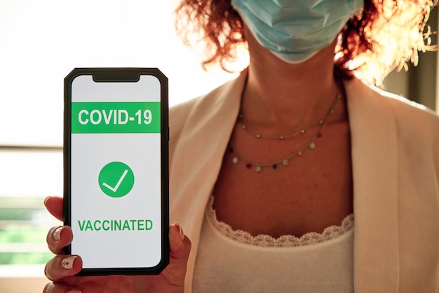 Una donna con maschera protettiva che mostra il certificato di vaccinazione covid-19 sullo smartphone