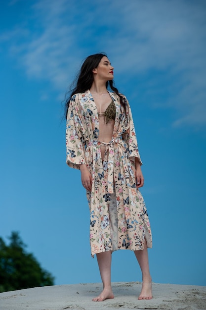 Una donna con un abito floreale si erge su una collina di fronte a un cielo blu.