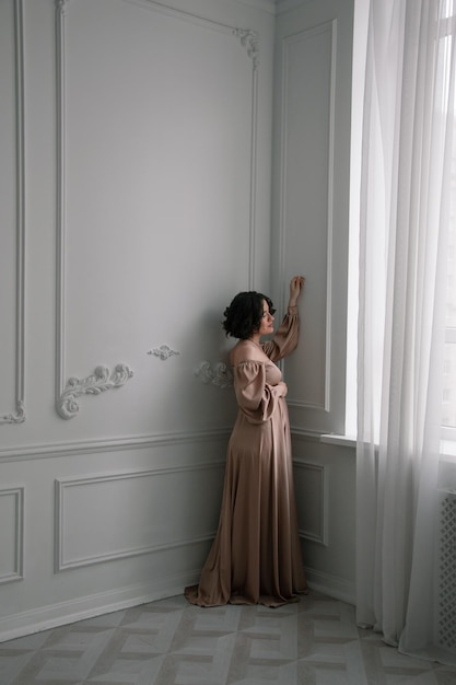 Una donna con un abito lungo è in piedi davanti a una finestra.