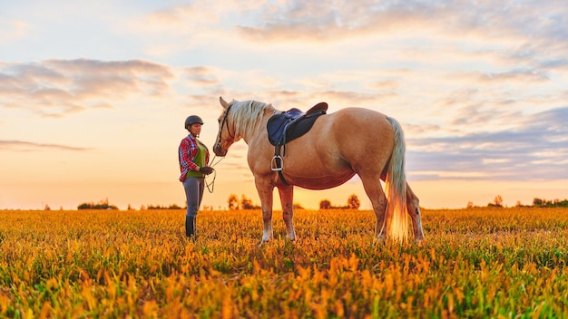 Una donna con un bellissimo cavallo palomino biondo cammina attraverso il campo al tramonto all'ora d'oro