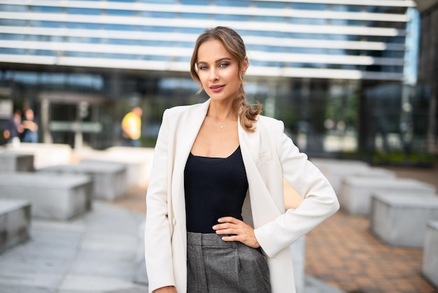 Una donna con un blazer bianco si trova di fronte a un edificio.