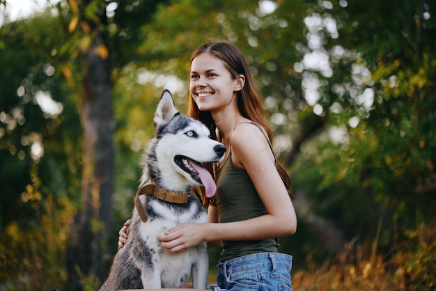 Una donna con un cane di razza husky sorride e accarezza affettuosamente il suo amato cane mentre cammina nella natura nel parco in autunno sullo sfondo del tramonto