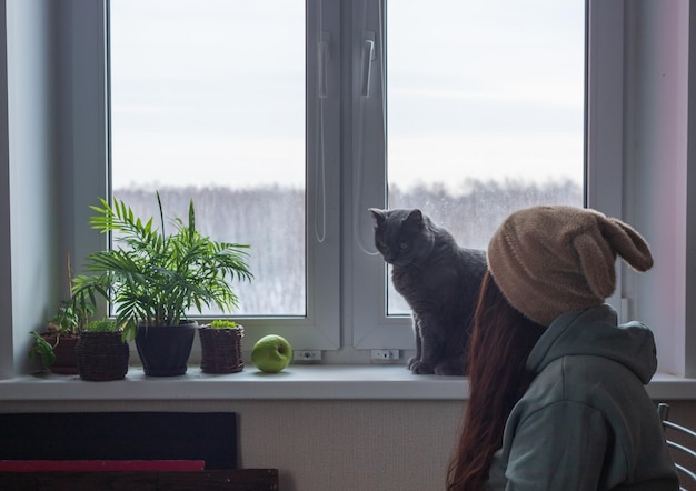 Una donna con un cappello con orecchie e capelli lunghi è seduta vicino alla finestra con il suo gatto