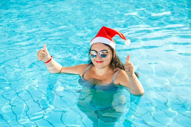 Una donna con un cappello da Babbo Natale in piscina festeggia il Natale e mostra la sua classe con la mano.