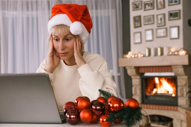 Una donna con un cappello da Babbo Natale si congratula con i parenti e gli amici su un laptop con il capodanno di Natale