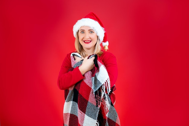 Una donna con un cappello da Babbo Natale su uno sfondo rosso stringeva al petto un plaid natalizio