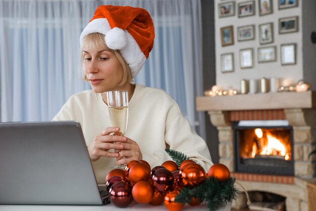 Una donna con un cappello da Babbo Natale tiene un bicchiere di champagne parenti e amici su un laptop con Natale