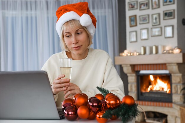 Una donna con un cappello da Babbo Natale tiene un bicchiere di champagne parenti e amici su un laptop con Natale