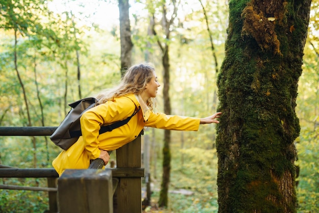 Una donna con un cappotto giallo e uno zaino cammina lungo una scala in legno godendosi il paesaggio autunnale nella foresta