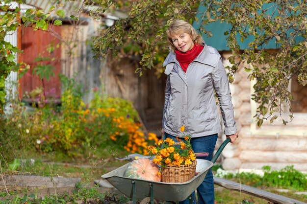 Una donna con un cesto è in giardino. Una donna di mezza età in jeans e giacca tiene la sua carriola in giardino.