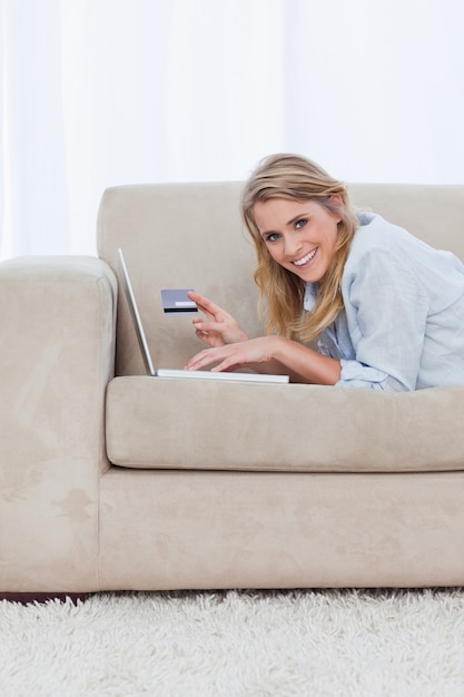 Una donna con un computer portatile sta guardando la fotocamera e in possesso di una carta bancaria