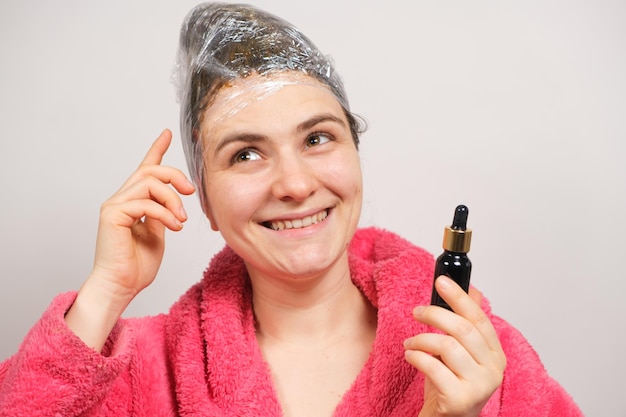 Una donna con un film in testa tiene in mano una bottiglia di olio per capelli naturale