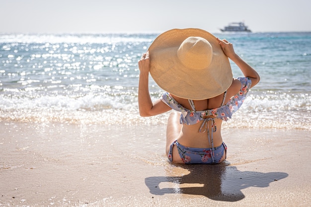 Una donna con un grande cappello prende il sole sulla spiaggia vicino allo spazio della copia del mare.