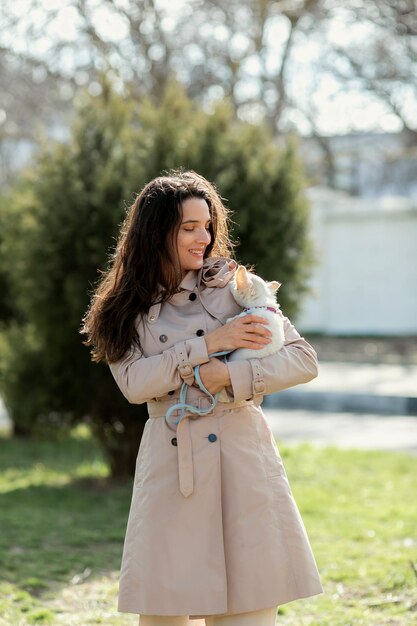 una donna con un impermeabile leggero cammina e gioca con un cagnolino bianco