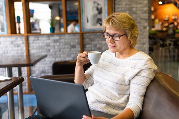 Una donna con un laptop sta lavorando in un ufficio. Una donna d'affari di mezza età siede in un caffè. Sorride e beve il suo tè