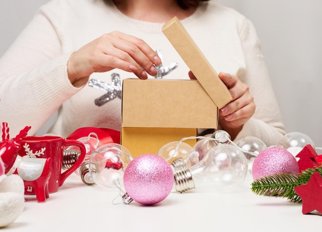 Una donna con un maglione bianco si siede al tavolo e avvolge i regali per Natale, preparandosi per le vacanze