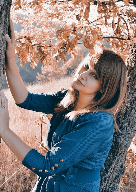 Una donna con un maglione blu si trova in un campo con un albero in primo piano.