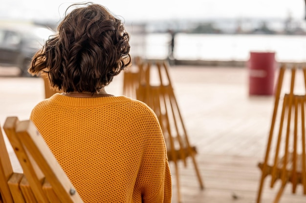 Una donna con un maglione giallo siede su un molo e guarda l'acqua.