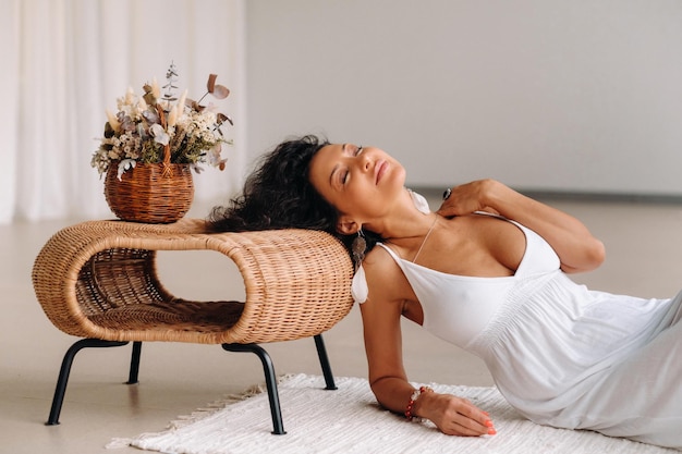 Una donna con un prendisole bianco in un interno luminoso giace su un tappeto bianco. Il concetto di relax.