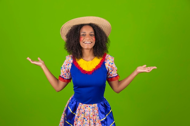 Una donna con un vestito blu con un nastro giallo e rosso e un cappello di paglia è in piedi davanti a un muro verde.