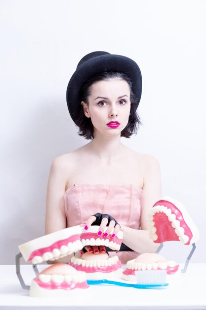 Una donna con un vestito e un cappello si siede a un tavolo e tiene un mockup dei suoi denti Foto di alta qualità