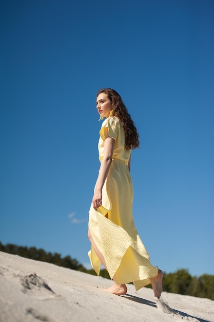 Una donna con un vestito giallo si trova su una duna di sabbia.