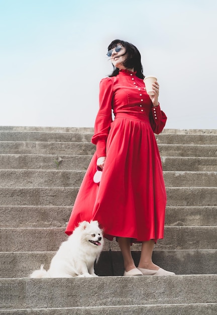 Una donna con un vestito rosso con una tazza di caffè e un piccolo cane bianco e soffice