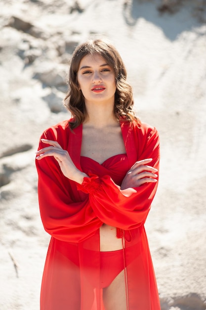 Una donna con un vestito rosso si trova di fronte a una spiaggia sabbiosa.